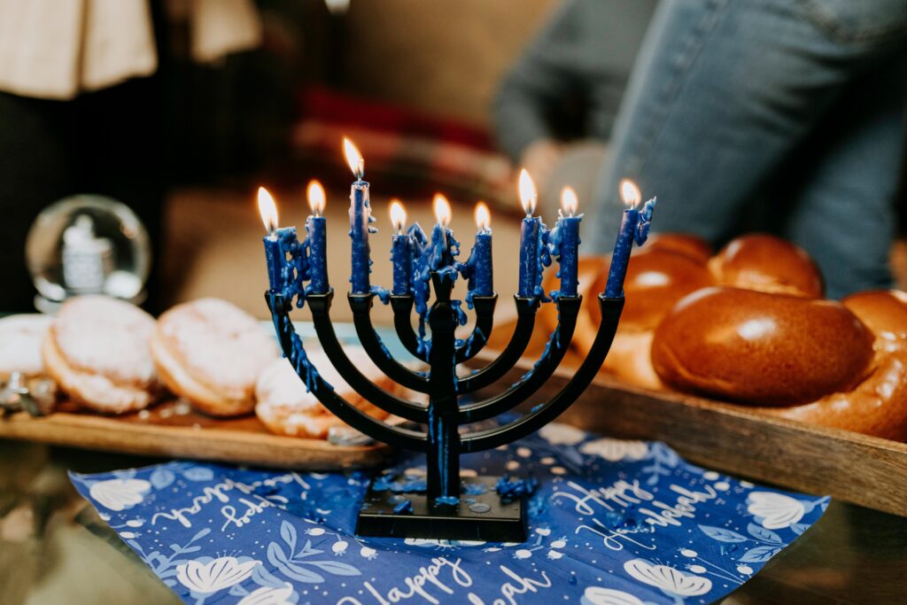 Lit menorah on a festive Hanukkah table with traditional foods like challah and sufganiyot.